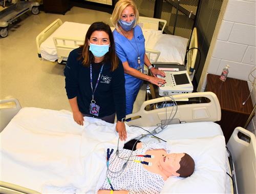 Two James Clemens High School health teachers surrounding a robotic patient in a classroom 